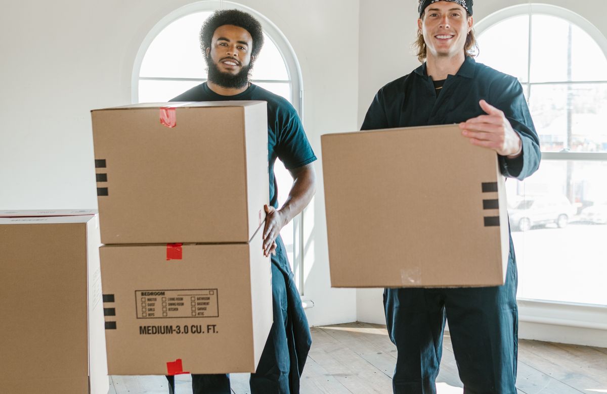 Two movers carrying packed cartons into a home in Mumbai